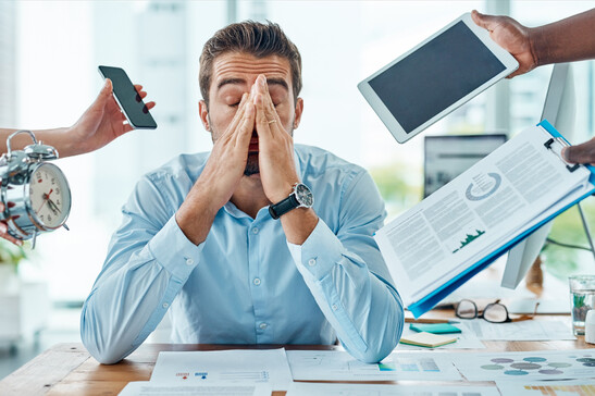 Un uomo alla scrivania sollecitato da molte incombenze foto iStock.